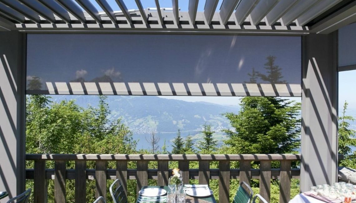 Gedeckter Esstisch unter einem Lamellendach mit seitlichem Screen und Blick auf den Vierwaldstättersee in Nidwalden.