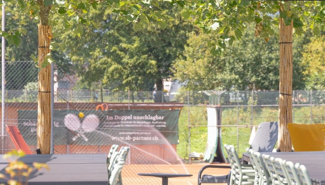 Blick aus dem Lamellendach beim Tennisclub Horw in Luzern – Sitzbereich mit Tischen und Stühlen, im Hintergrund die Tennisplätze.