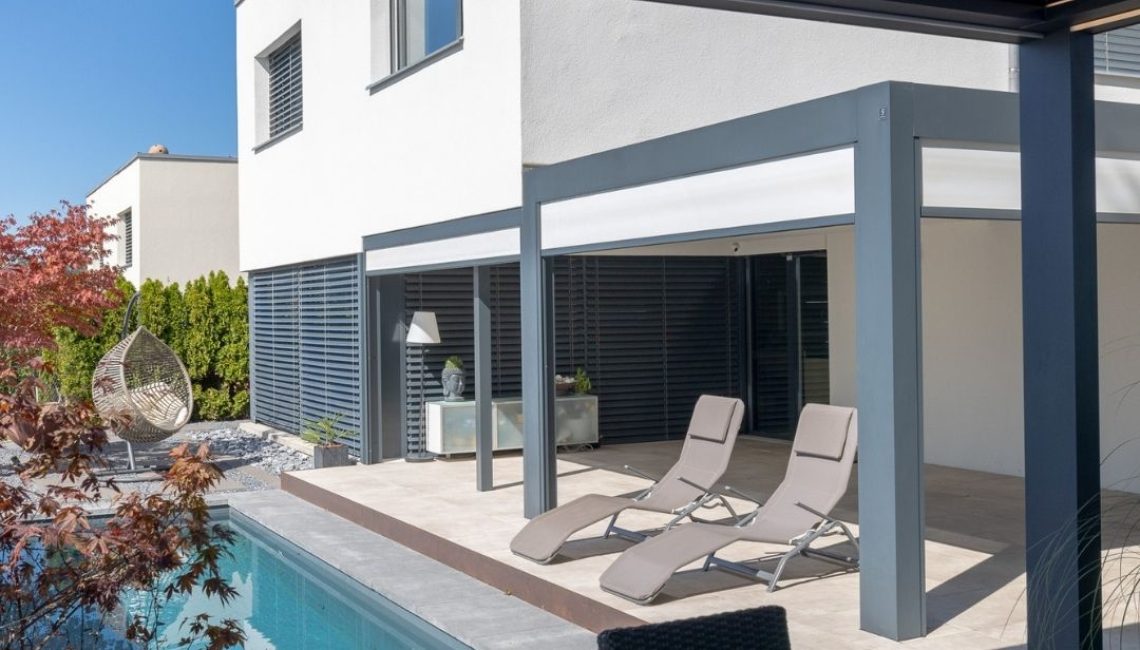 SKL 140 Lamellendach über Poolterrasse – zwei Liegestühle im Schatten, moderner Outdoor-Bereich mit Hängesessel und japanischem Ahorn.