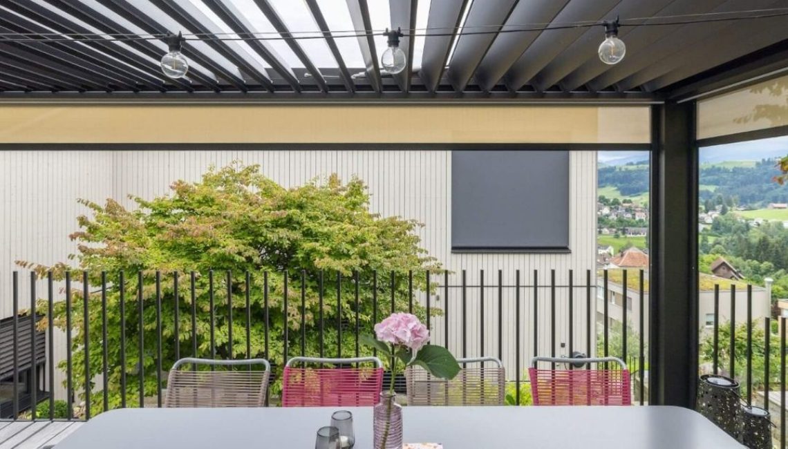 Innenansicht des Lamellendachs in Teufen Appenzell mit modernem Esstisch, farbigen Stühlen und Blick ins Grüne.