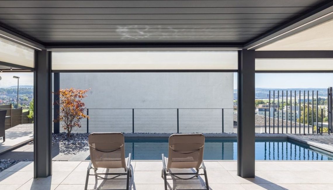 SKL 140 Lamellendach über Poolterrasse – zwei Liegestühle mit Blick aufs Wasser und Panorama im Hintergrund.