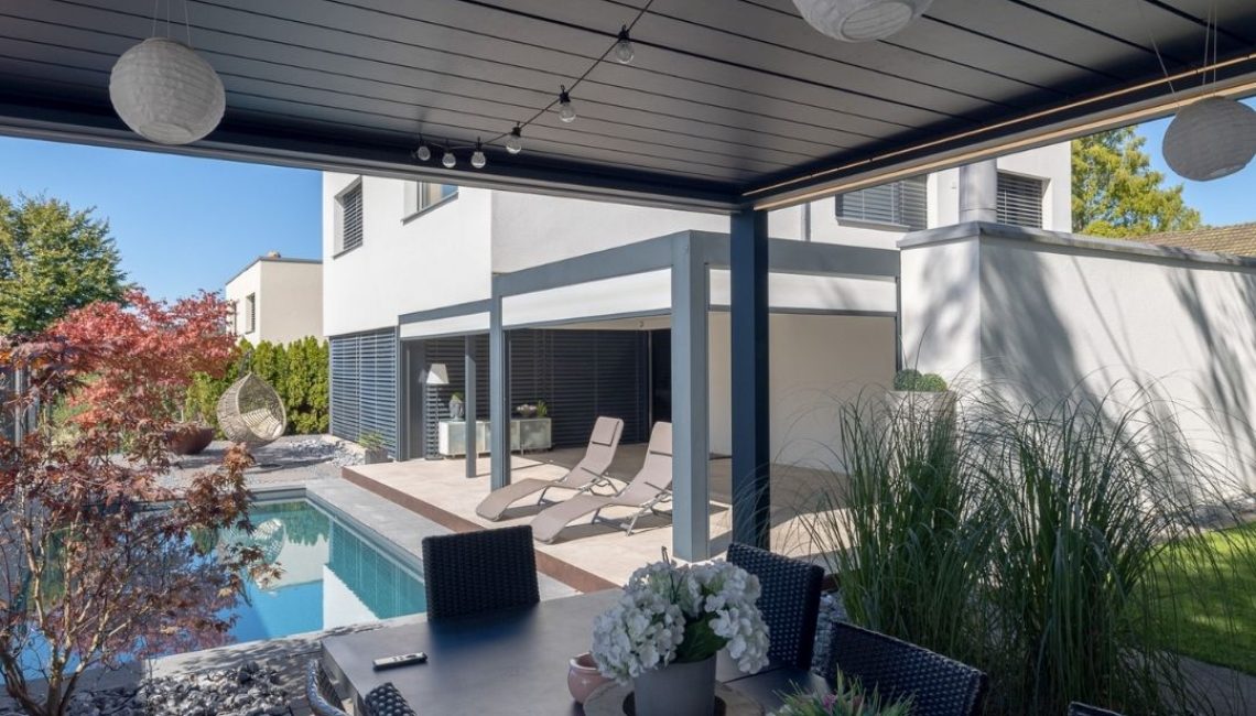 Blick von der gedeckten Terrasse mit SKL 100 Lamellendach auf den Poolbereich mit SKL 140 Lamellendach – zwei hochwertige Überdachungen mit Schneelast bis 300 kg/m².