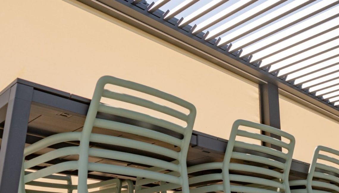 Detailaufnahme unter dem Lamellendach beim Tennisclub Horw in Luzern – moderne Stühle und Tisch unter geöffneten Lamellen mit geschlossenen Senkrechtmarkisen.