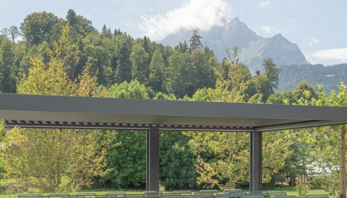 Lamellendach beim Tennisclub Horw in Luzern – überdachter Sitzbereich mit langen Tischen und Stühlen, im Hintergrund der Pilatus.