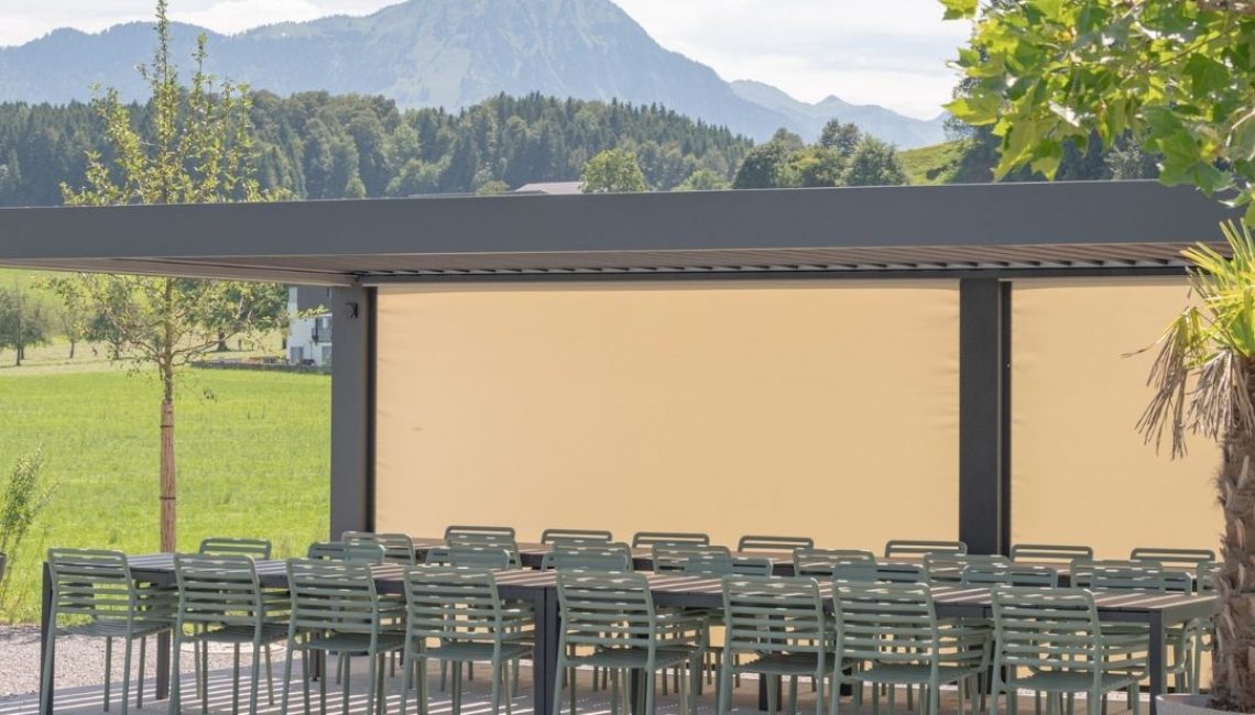 Lamellendach beim Tennisclub Horw in Luzern mit geschlossenen Seitenmarkisen und langen Tischreihen vor Bergpanorama.