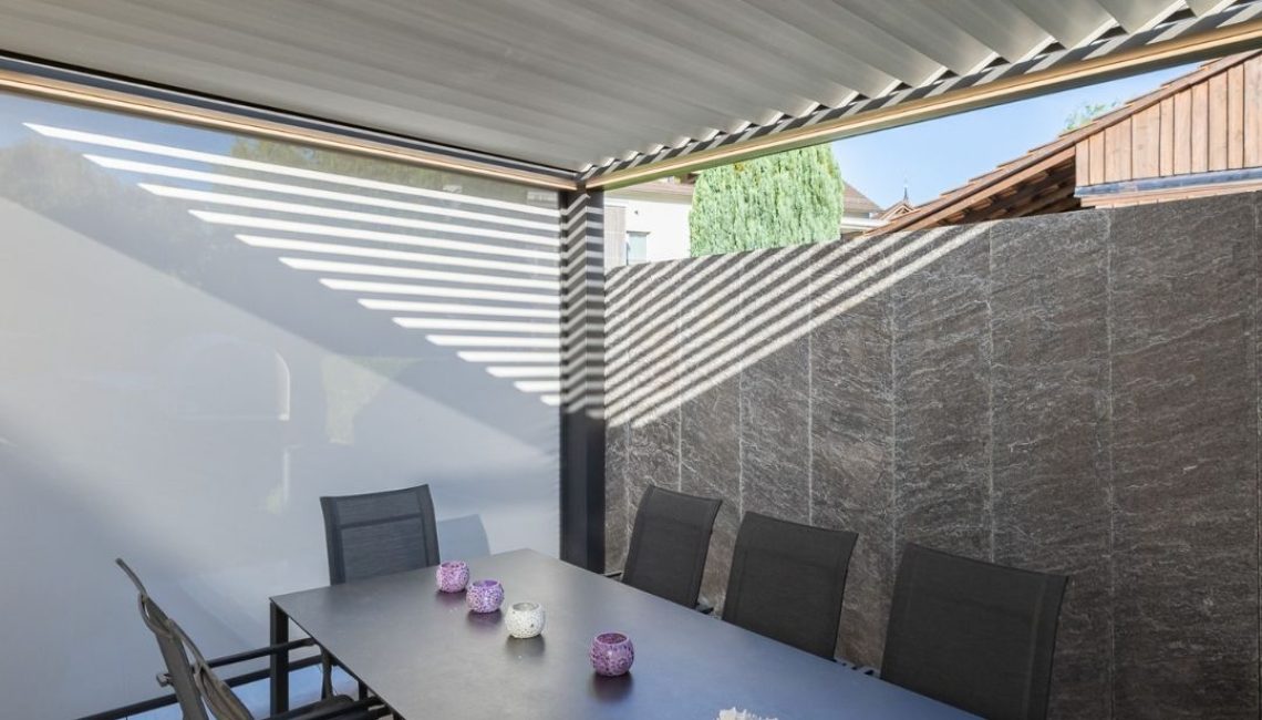 Essbereich unter einem geschlossenen Lamellendach mit seitlichem Sichtschutz und moderner Möblierung in ehrendingen Aargau.