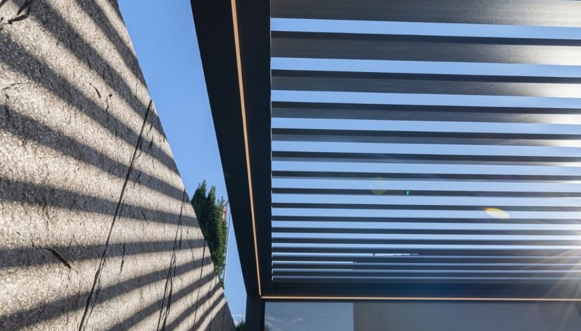 Detailaufnahme eines modernen Lamellendachs in Ehrendingen Aargau, das Sonnenlicht in gleichmässigen Linien auf eine Steinmauer wirft.