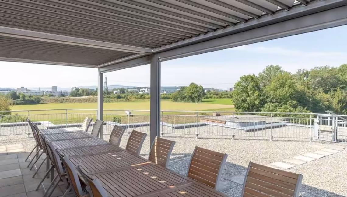 Lange Tischreihe unter einem SKL 140 Lamellendach in Glattbrugg Zürich, Schneelast bis 300 kg/m², ideal für Firmen- und Gemeinschaftsnutzung.