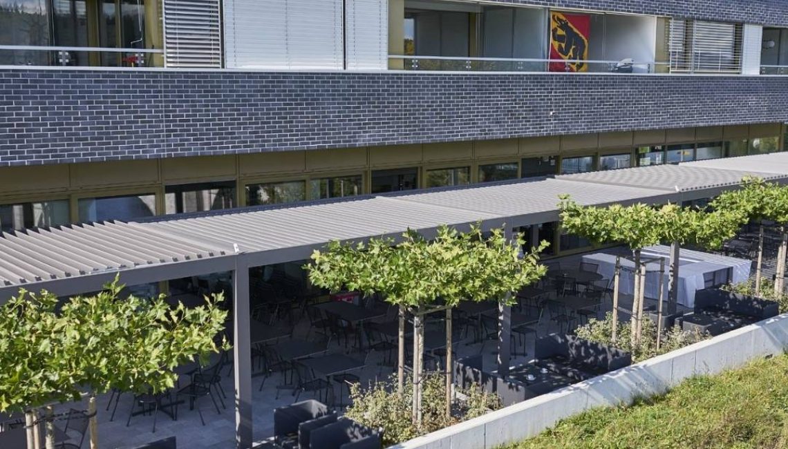 Grosszügiges SKL 100 Lamellendach in Hinterkappelen Bern, bietet auf der gesamten Terrasse eines Gebäudes zuverlässigen Sonnen- und Wetterschutz.