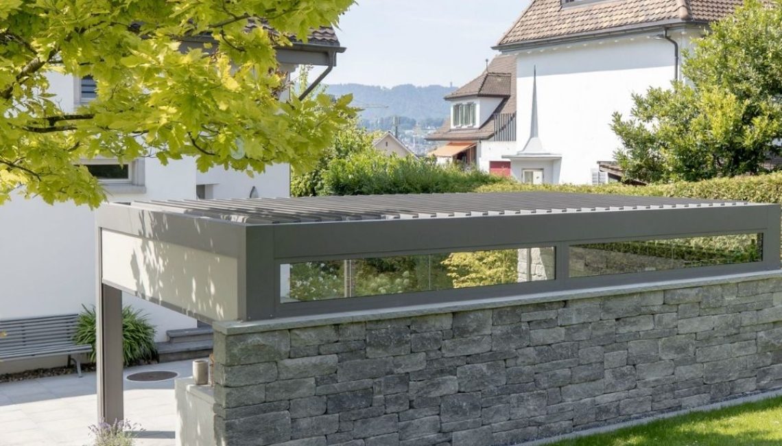 Rückansicht des SKL 140 Lamellendachs in Küsnacht Zürich, integriert in eine Natursteinmauer und umgeben von einem gepflegten Garten.