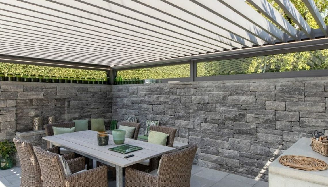 Essbereich unter dem SKL 140 Lamellendach in Küsnacht Zürich mit eleganter Steinmauer und gemütlicher Sitzgruppe für gesellige Stunden im Freien.