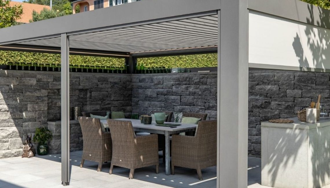 SKL 140 Lamellendach in Küsnacht Zürich mit Natursteinmauer und integriertem Essbereich mit Gartentisch und Korbstühlen.