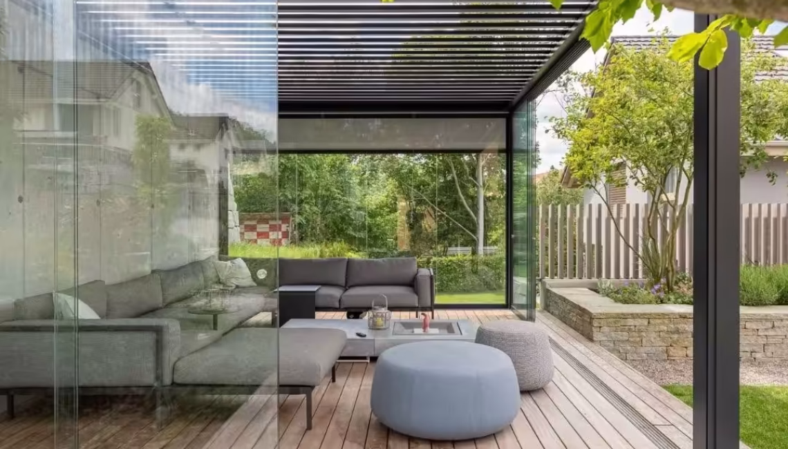 SKL 100 Lamellendach mit Glaswänden in Malters, Luzern – moderner Outdoor-Wohnraum mit gemütlicher Lounge und Holzdeck.