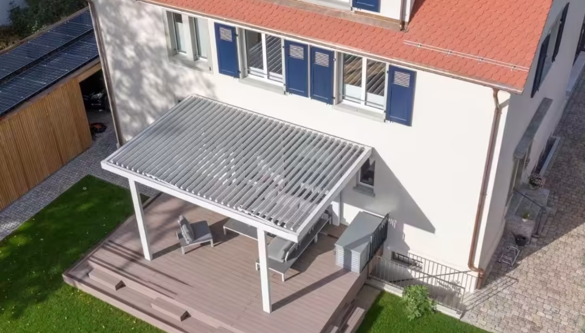 SKL 100 Lamellendach in Riehen Basel-Land, montiert über einer erhöhten Holzterrasse mit moderner Lounge.