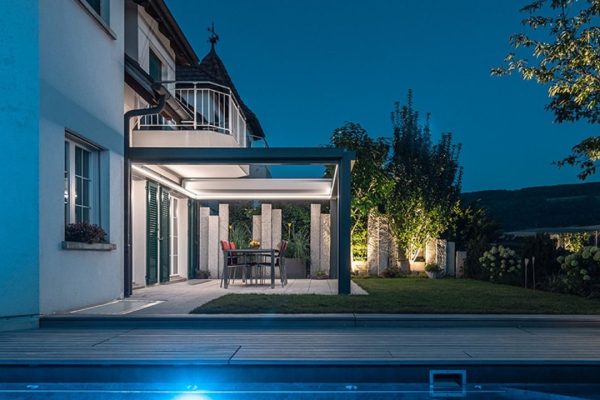 SKL 150 Panorama Lamellendach bei Nacht mit seitlich verfahrbaren Lamellen und integrierter LED-Beleuchtung, Terrasse am Pool.