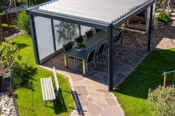 Vogelperspektive auf ein SKL 50 Lamellendach mit geschlossenen Lamellen und windfesten Seitenmarkisen im Garten.