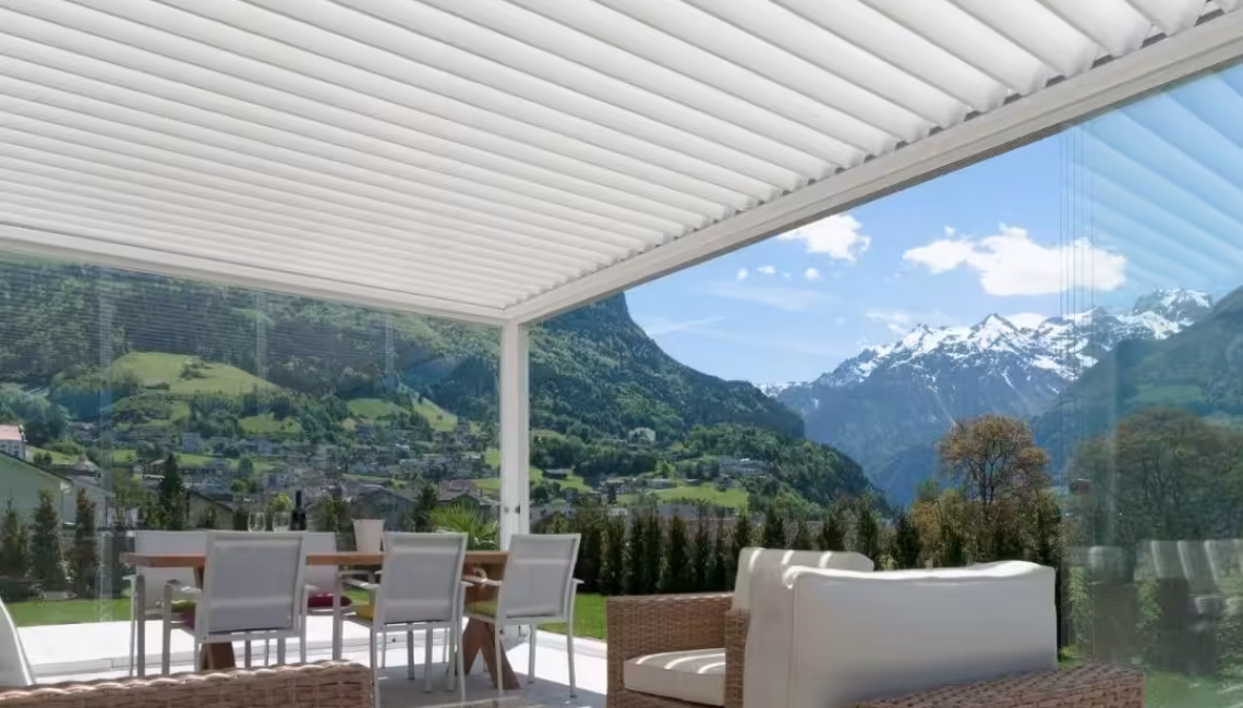 SKL 100 Lamellendach in Schattdorf, Uri – weisse Konstruktion mit Glaswänden und 300 kg/m² Schneelast, stilvoll eingerichteter Outdoorbereich mit Blick auf die Schweizer Alpen.