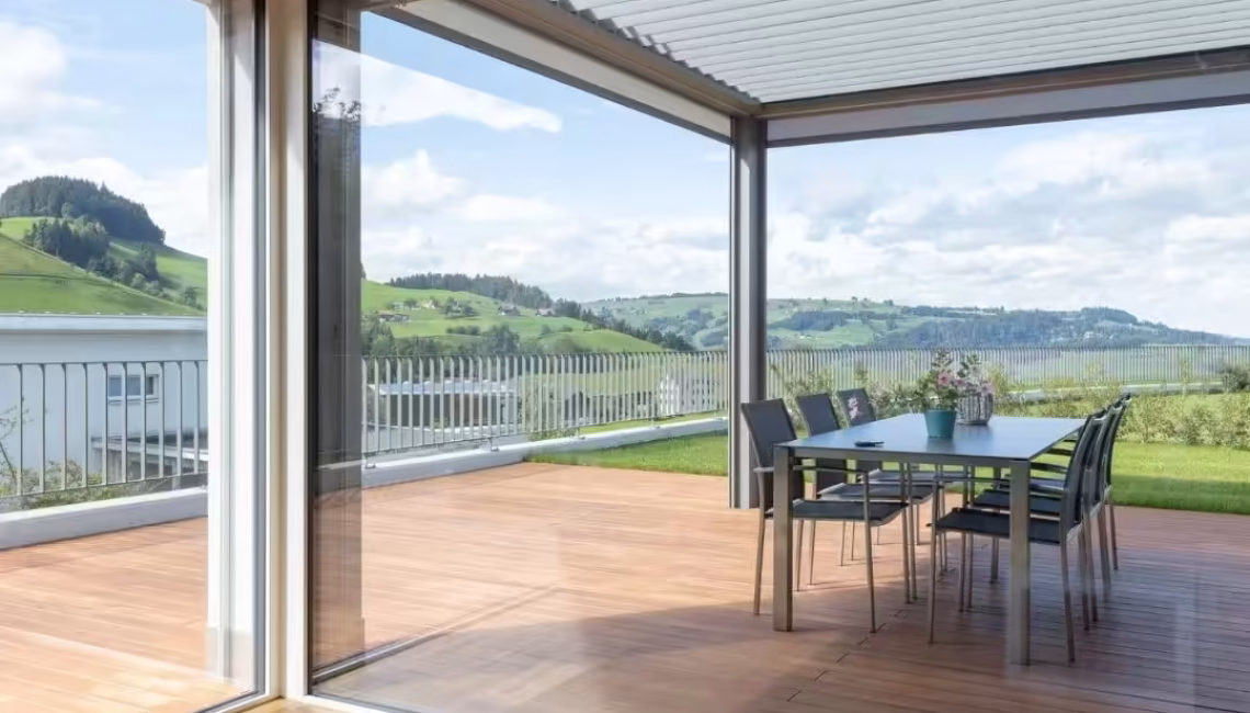 SKL 140 Lamellendach in Schwarzenberg, Luzern – Blick aus dem Wohnraum auf die gedeckte Terrasse mit Esstisch und offener Landschaft.