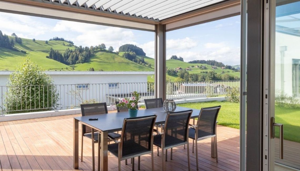 SKL 140 Lamellendach in Schwarzenberg, Luzern – geschlossene Lamellen über einer Holzterrasse mit Esstisch und Blick auf die hügelige Landschaft.