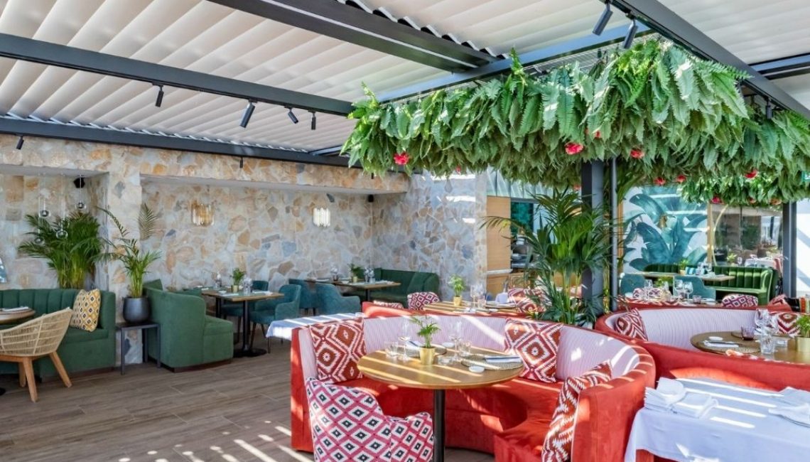 SKL 100 Lamellendach im Restaurant Al Porto in Thal St. Gallen mit elegantem Licht- und Schattenspiel über farbenfrohen Sitzgruppen.