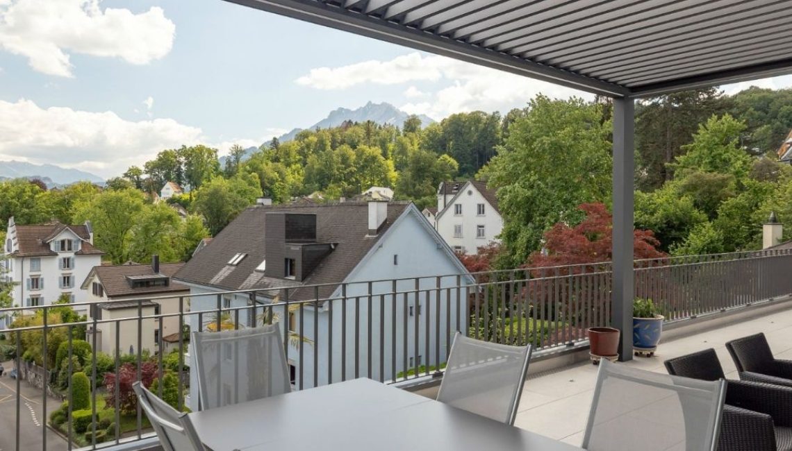SKL 140 Lamellendach auf einer grosszügigen Dachterrasse in Luzern mit Esstisch, Lounge-Bereich und Blick ins Grüne sowie auf den Pilatus.