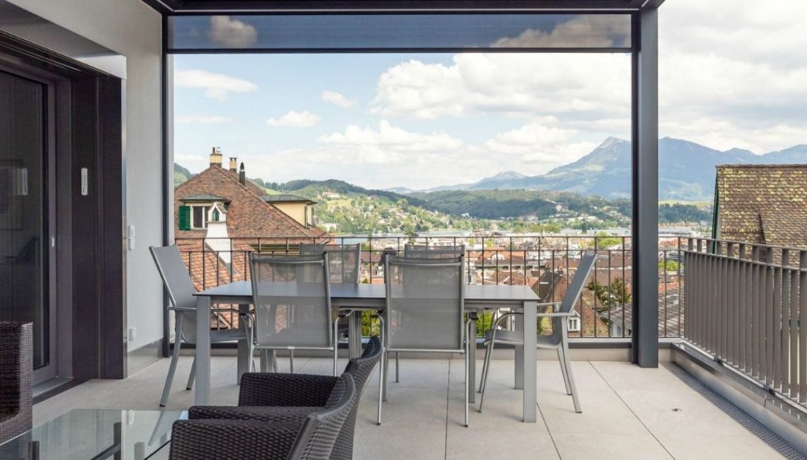 SKL 140 Lamellendach auf einer modernen Dachterrasse in Luzern mit Esstisch, Lounge-Bereich und Blick auf die umliegenden Berge.