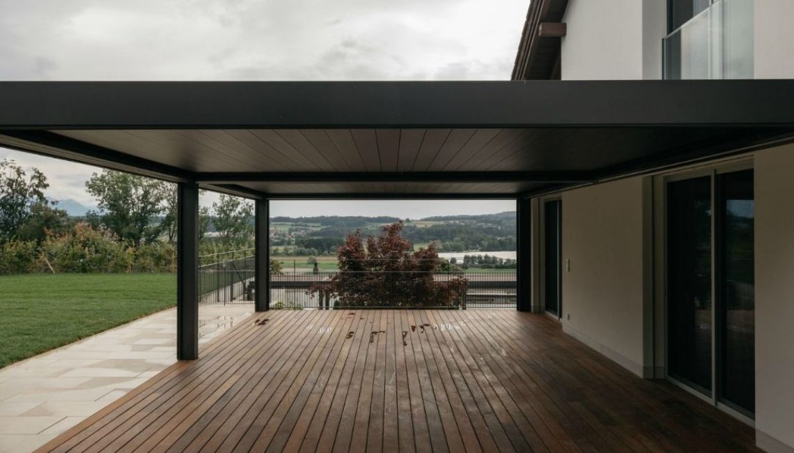 Grosszügige Terrasse in Zug mit SKL 140 Lamellendach und Holzdeck, Blick auf die Landschaft im Hintergrund.