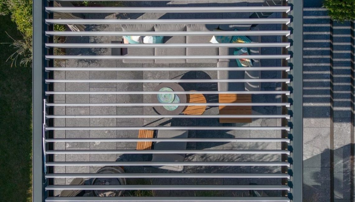 Draufsicht auf ein modernes Lamellendach mit darunterliegendem Lounge-Bereich im Garten.