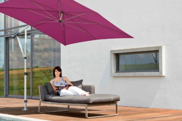 Moderner MEZZO Sonnenschirm in kräftigem Violett neben einem Pool, spendet Schatten für eine stilvolle Liege mit entspannter Person.