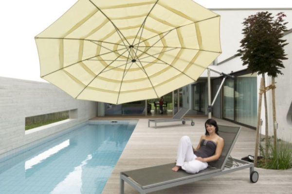 Moderner MEZZO Sonnenschirm in hellem Beige über einer Poolliege, seitlich geneigt für optimalen Schatten.