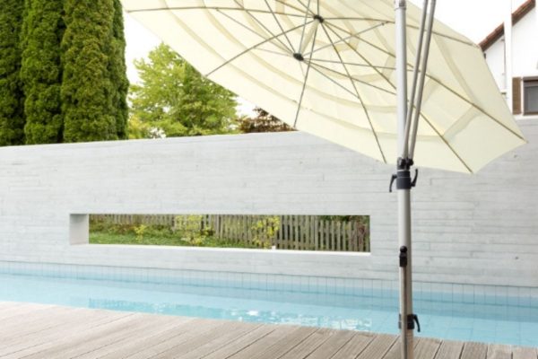 Seitlich geneigter MEZZO Sonnenschirm in heller Farbe auf einer modernen Poolterrasse mit Holzdeck.