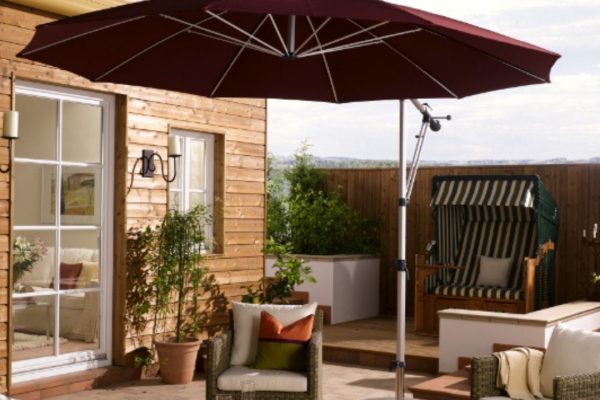 Eleganter MEZZO Sonnenschirm in Dunkelrot auf einer stilvollen Terrasse mit Lounge-Möbeln und Strandkorb im Hintergrund.
