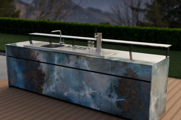 Exklusive Theiss Outdoor-Bar mit Zapfanlage, Spülbecken und modernem Design in blauen Steinfronten vor Alpenkulisse bei Sonnenuntergang.