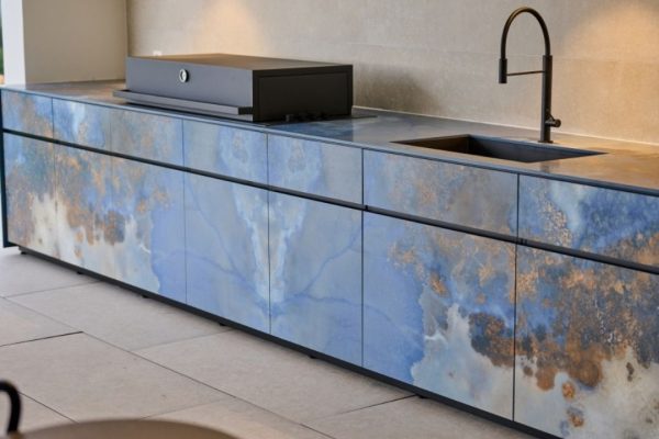 Exklusive Outdoor Küche mit modernem Design in Blau- und Naturtönen, ausgestattet mit Grill und Spülbecken.