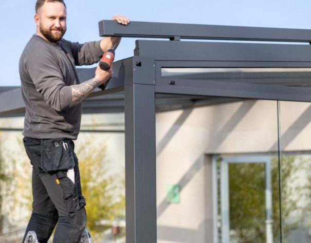 Montage mit Erfahrung Thermogreen Monteur steht auf einer Leiter und montiert präzise eine Aluminium-Überdachung.