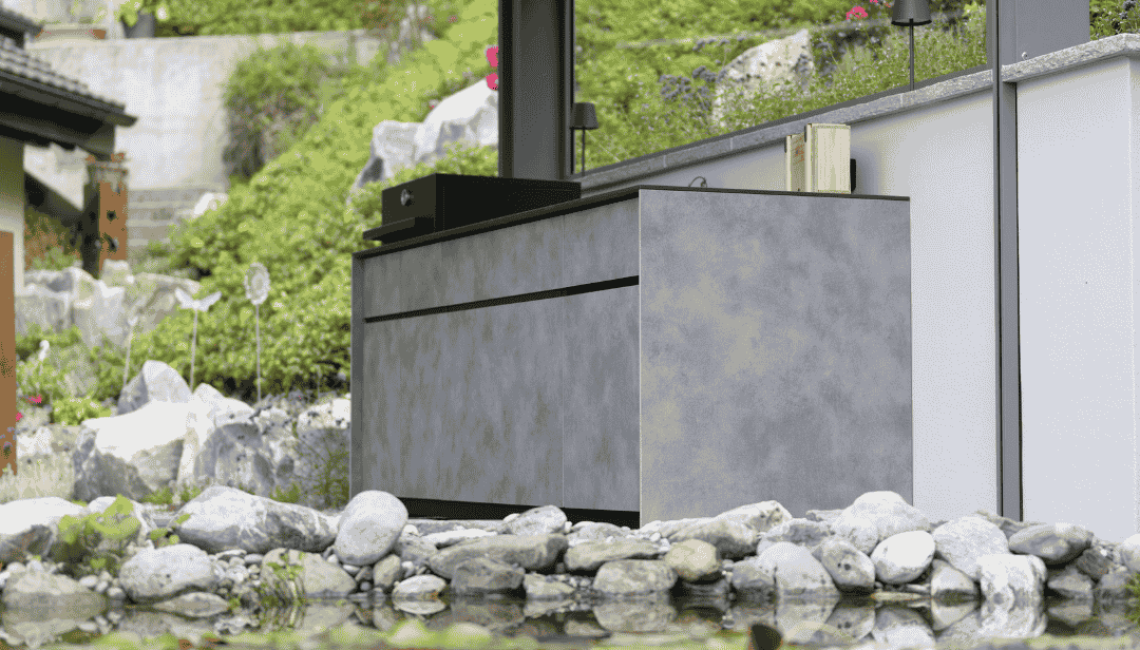 Aussenküche mit Keramikarbeitsfläche unter Überdachung mit Spiegelung im Gartenteich