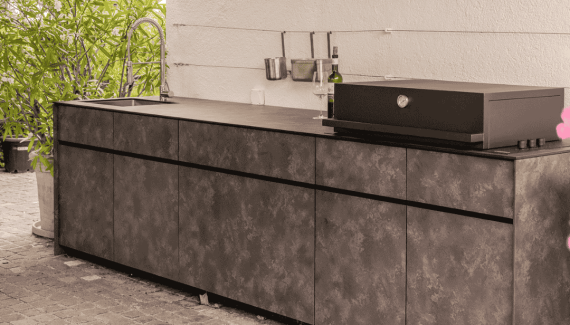 Aussenküche Theiss Avers in Stäfa mit HPL Stone ME Oberfläche, integriertem Grill und Spülbecken entlang einer Hauswand im Gartenbereich