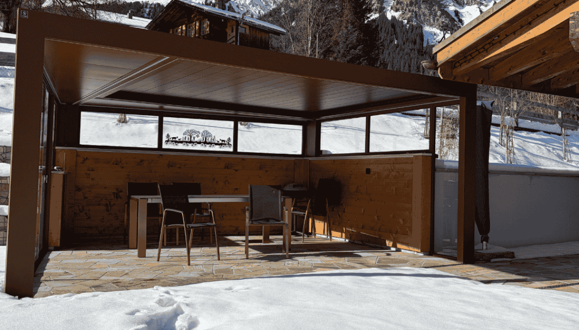 Lamellendach mit seitlichen Festelementen und Verglasung auf einer Terrasse in Lenk im Simmental, umgeben von Schnee und alpiner Berglandschaft.