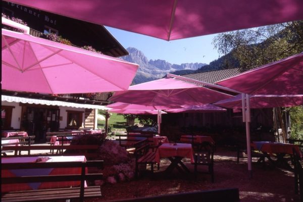 Grosse pinke RIALTO Sonnenschirme spenden Schatten auf einer Alpenterrasse mit gedeckten Tischen.