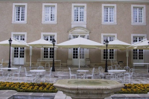 Helle RIALTO Sonnenschirme spenden Schatten auf der Terrasse eines historischen Hauses mit klassischem Ambiente.
