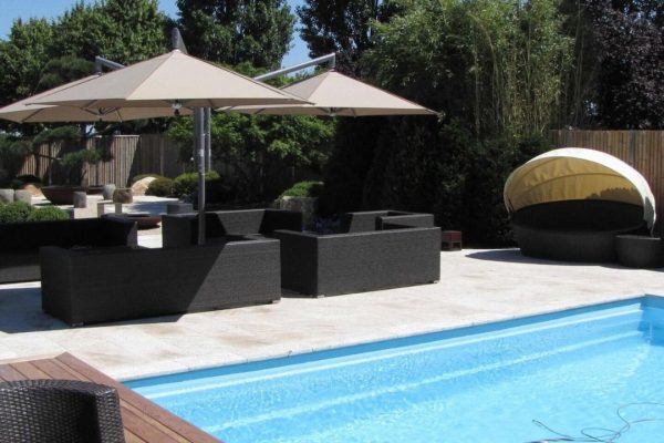 Zwei beige RIALTO Sonnenschirme spenden Schatten über einer modernen Lounge am Pool.