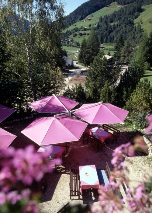 RIALTO Sonnenschirme – Klassiker für die Gastronomie Pinkfarbene RIALTO Sonnenschirme auf einer Restaurantterrasse mit Blick auf die Berge.