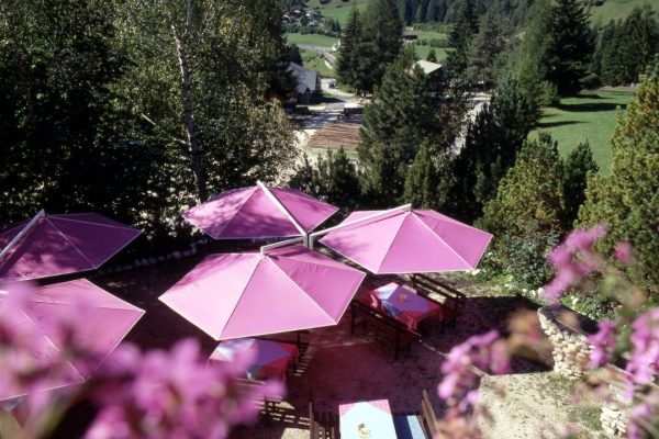 Pinkfarbene RIALTO Sonnenschirme auf einer Restaurantterrasse mit Blick auf die Berge.