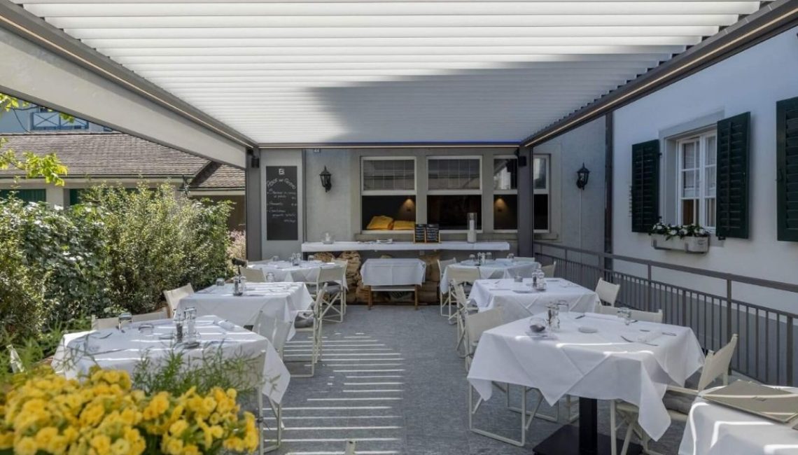 Gedeckte Terrasse mit Lamellendach im Restaurant Küsnacht, elegant eingedeckte Tische und angenehme Atmosphäre.