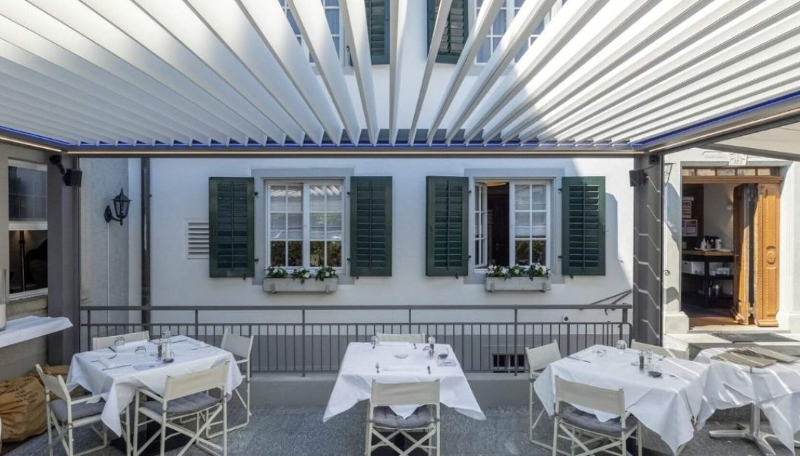 Offenes Lamellendach über der Restaurantterrasse in Küsnacht mit elegant eingedeckten Tischen.