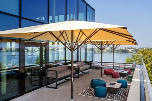 Gelbe SCHATTELLO Grossschirme auf einer modernen Hotelterrasse mit Lounge-Möbeln und Blick auf den See.