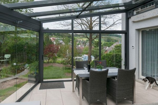 Wintergarten mit Glasdach SGL 2 und umlaufenden Glaswänden, geprüft bis 380 kg/m² Schneelast, sturmsicher und lichtdurchflutet mit Blick in den Garten.