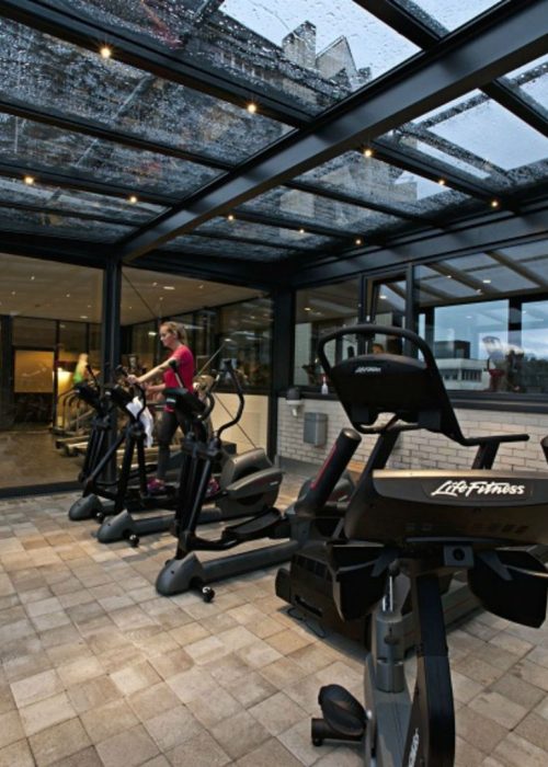 Glasdächer – Schutz mit voller Transparenz Glasdach als Überdachung eines Fitnessbereichs mit Outdoor-Trainingsgeräten, kombiniert Schutz und Offenheit.