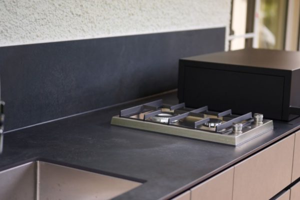 Detailaufnahme einer Valsot Outdoor-Küche mit dunkler Keramik-Arbeitsfläche, integriertem Gas-Kochfeld und Edelstahlspüle.