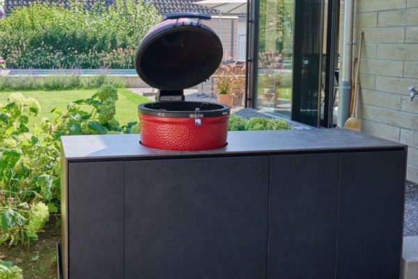Outdoor-Küche Valsot mit integriertem rotem Keramikgrill und nahtlosen Frontpaneelen im modernen Gartenambiente.